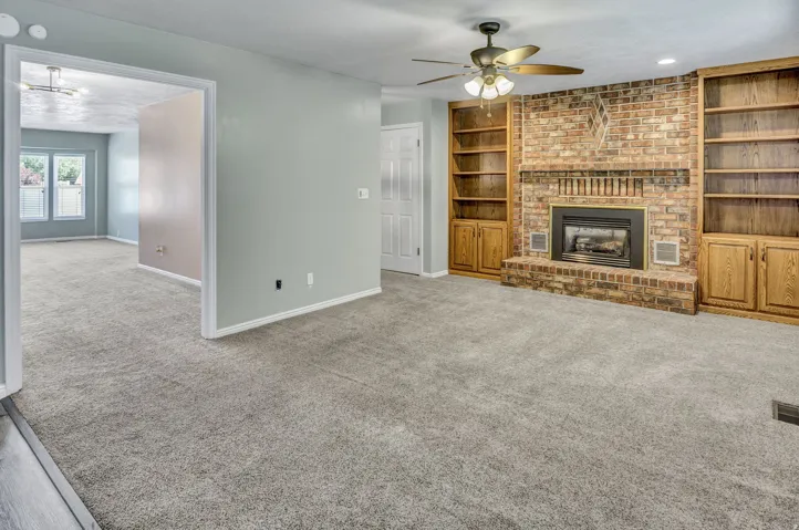 Spacious living area featuring a brick fireplace with a black insert, flanked by built-in wooden bookshelves and cabinetry
