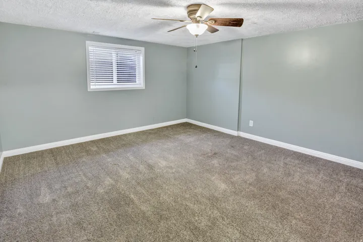 Carpeted interior room featuring light gray walls, white trim, a single window with blinds, and a ceiling fan with light fixture