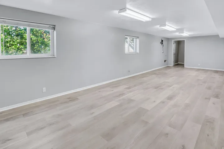 Spacious room featuring light-toned wood-finish flooring, white baseboards, and neutral gray walls