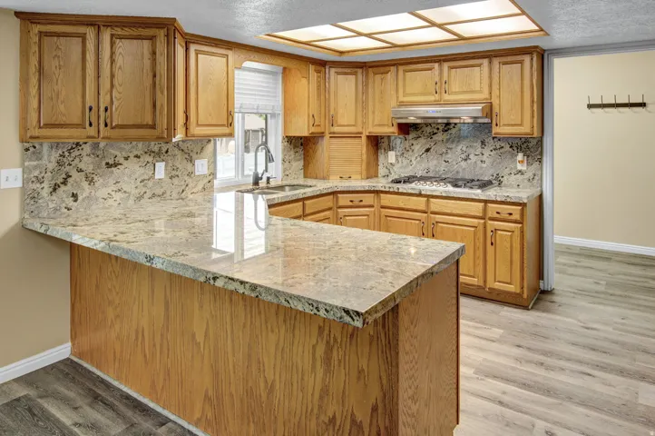 Kitchen featuring light wood cabinetry, stone countertops, integrated gas range with overhead ventilation, and a built-in sink