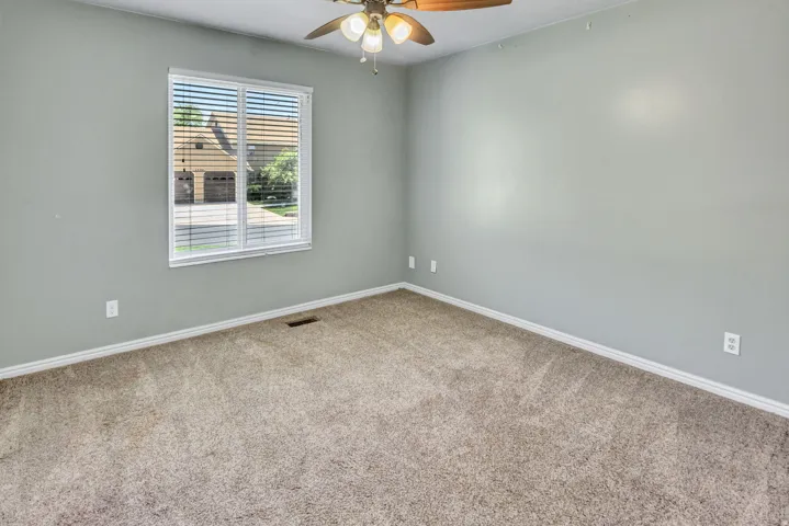 Carpeted room featuring light gray walls, a ceiling fan with integrated lighting, and a window with blinds