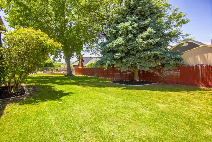Expansive lawn with mature trees and a red chain-link fence