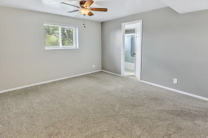 Spacious room featuring light gray wall paint, carpeting, and a ceiling fan with light fixture