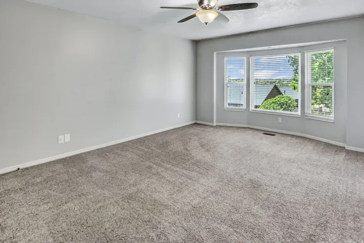 Carpeted room featuring a bay window with blinds, a ceiling fan with integrated lighting, and light gray painted walls