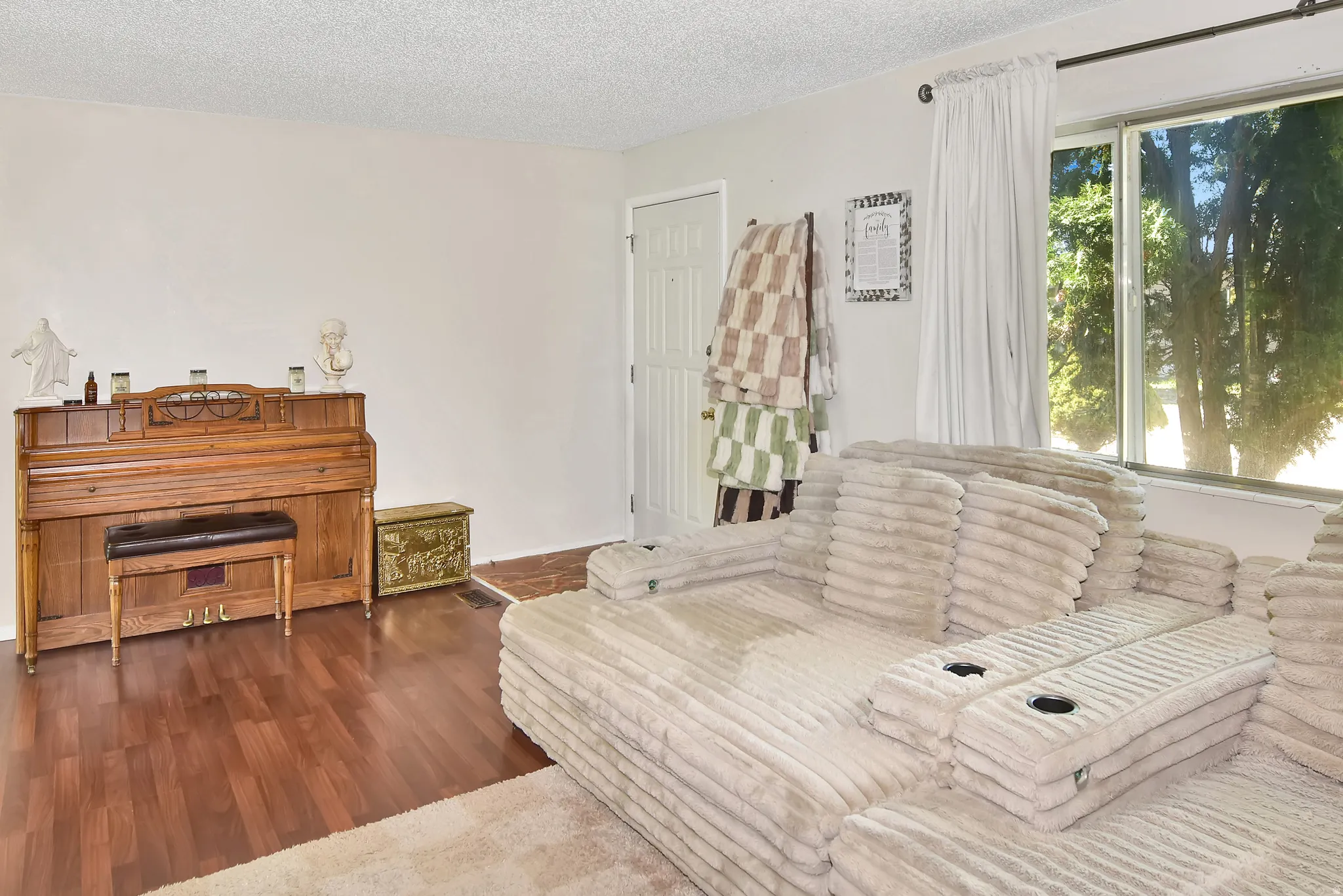Living area featuring wood-finish flooring, white painted walls, and a large window with white curtain panels