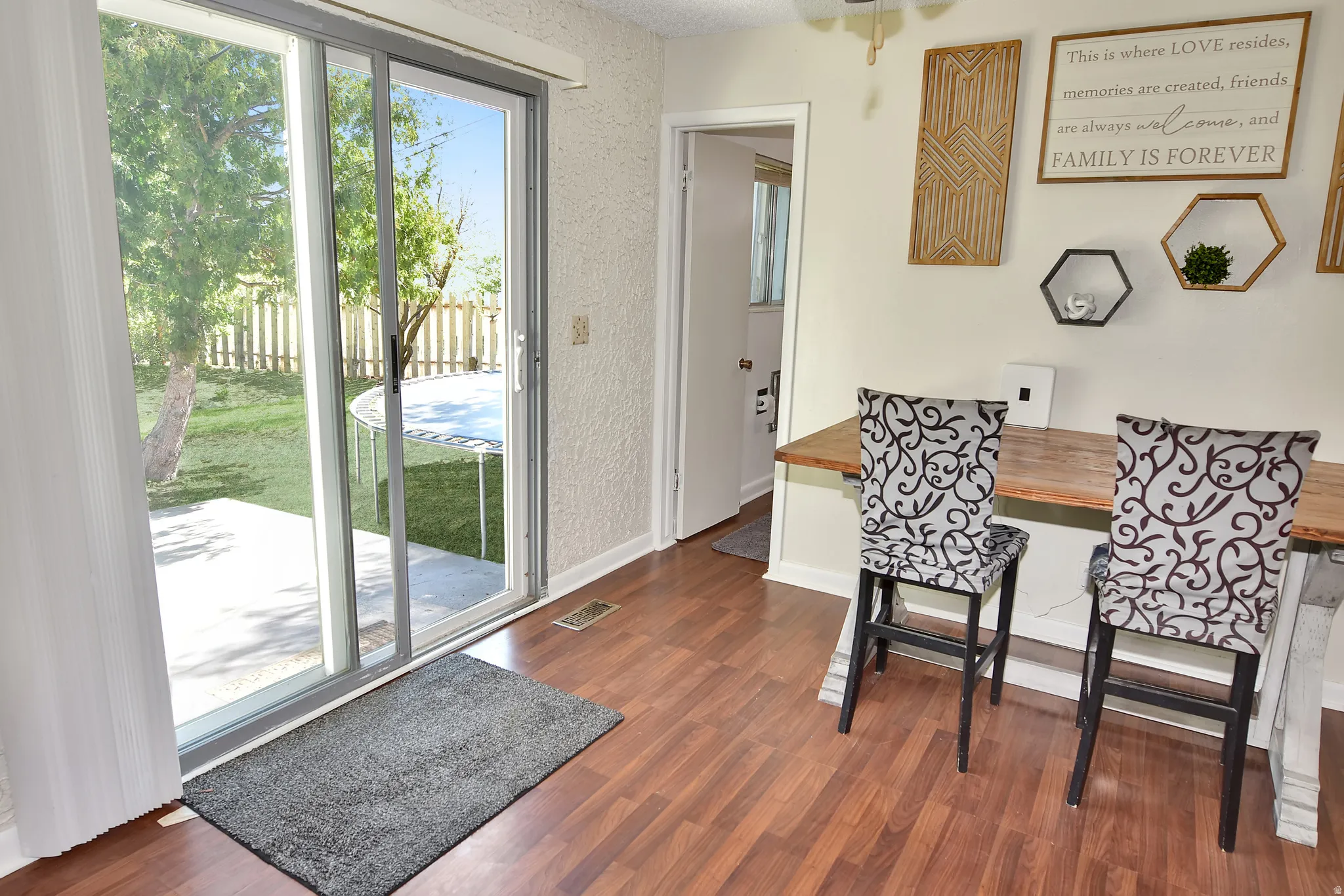 Sliding glass door opening to a concrete patio and a fenced backyard with mature trees