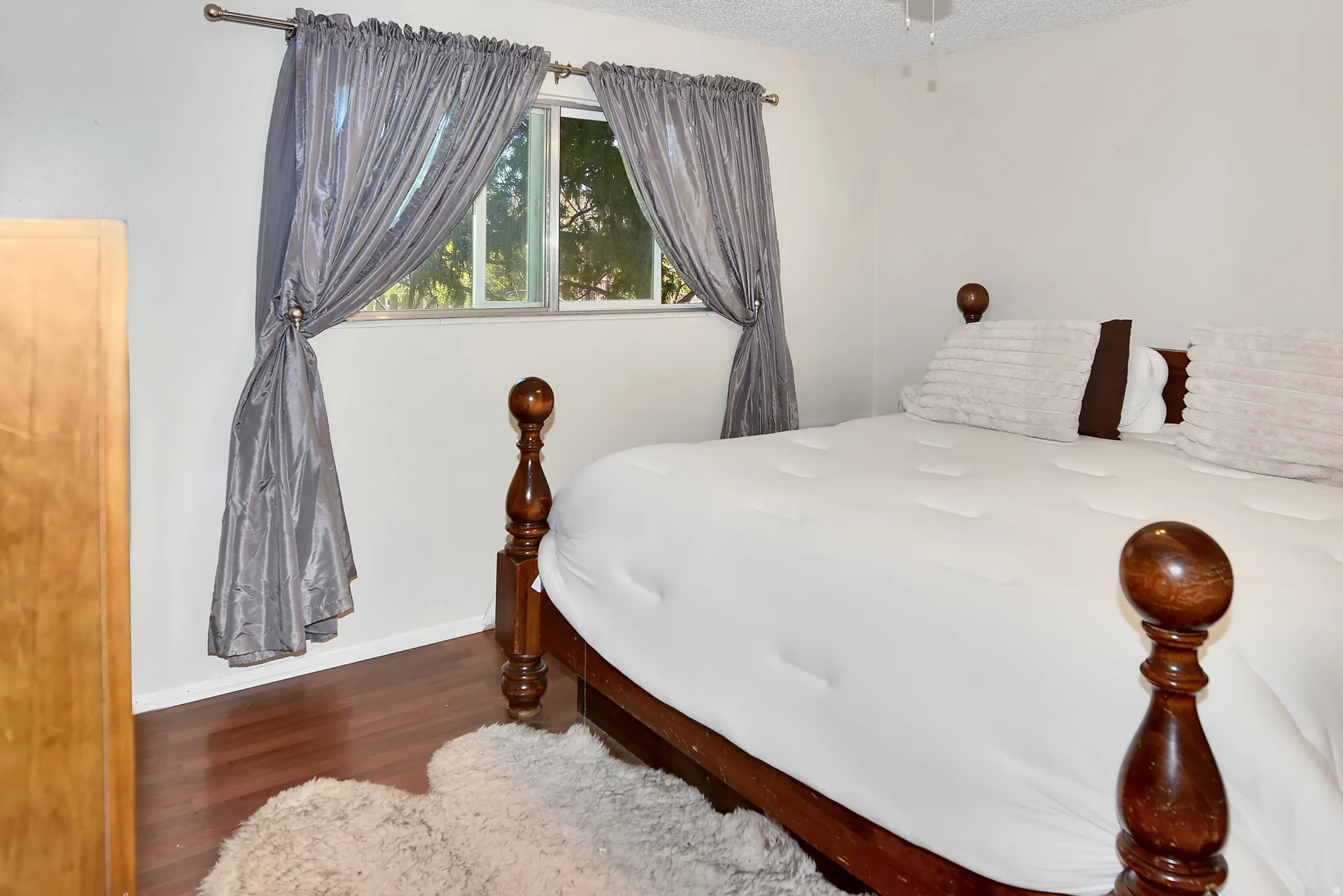 Bright bedroom featuring hardwood-finish flooring, white walls, and a window with exterior tree coverage