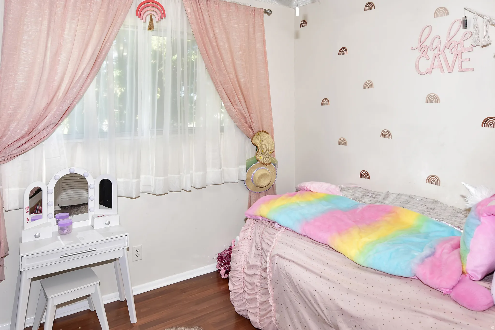 Interior room featuring wood-finish flooring, light-toned walls, and a window with sheer and fabric window treatments
