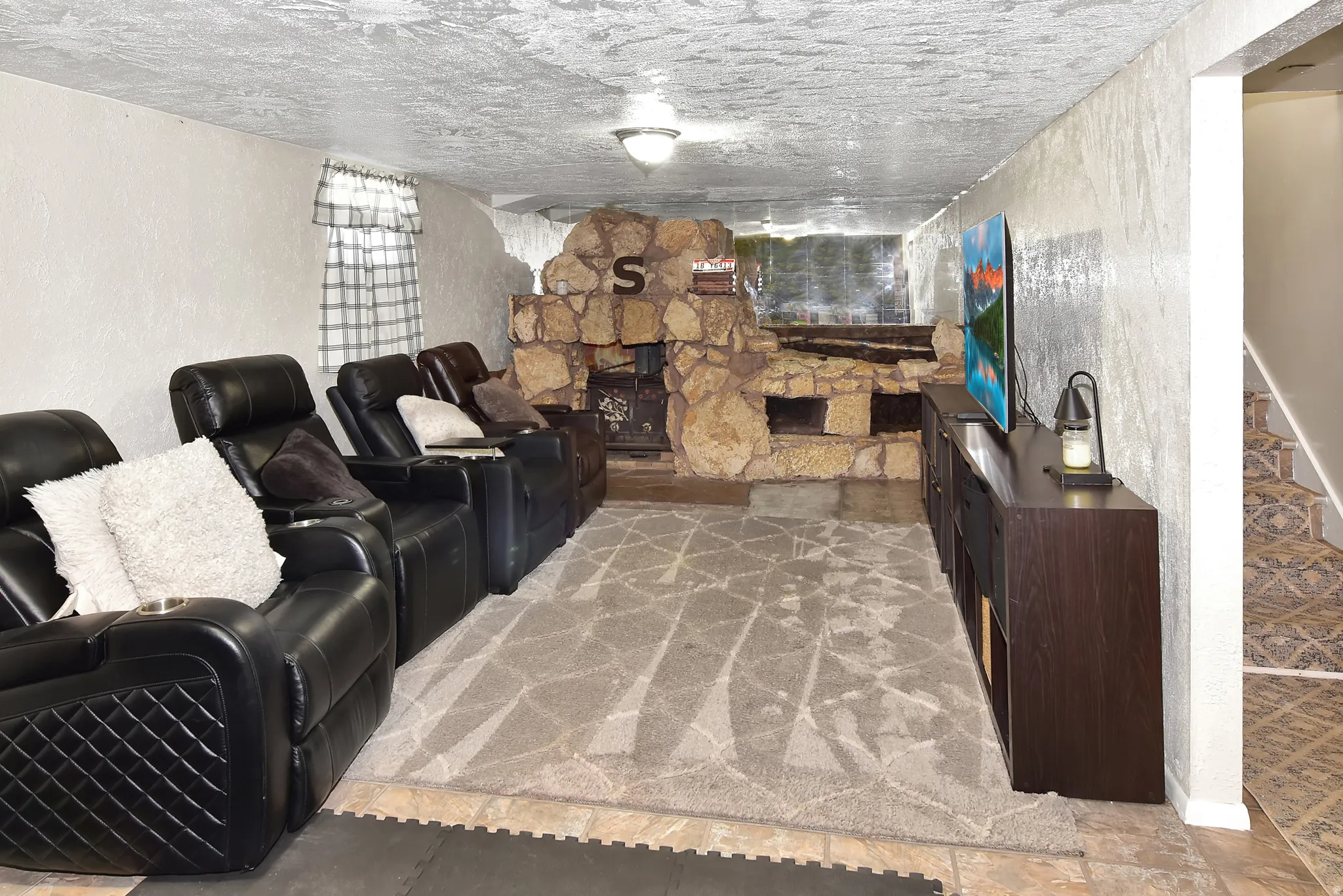 Spacious room featuring a stone-faced fireplace with hearth, textured wall finishes, and a decorative ceiling