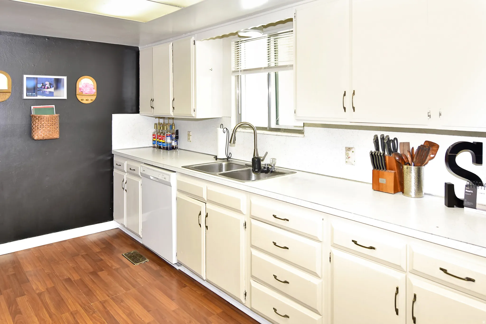 Kitchen featuring wood-finish flooring, white cabinetry, a double basin stainless steel sink, and a white dishwasher