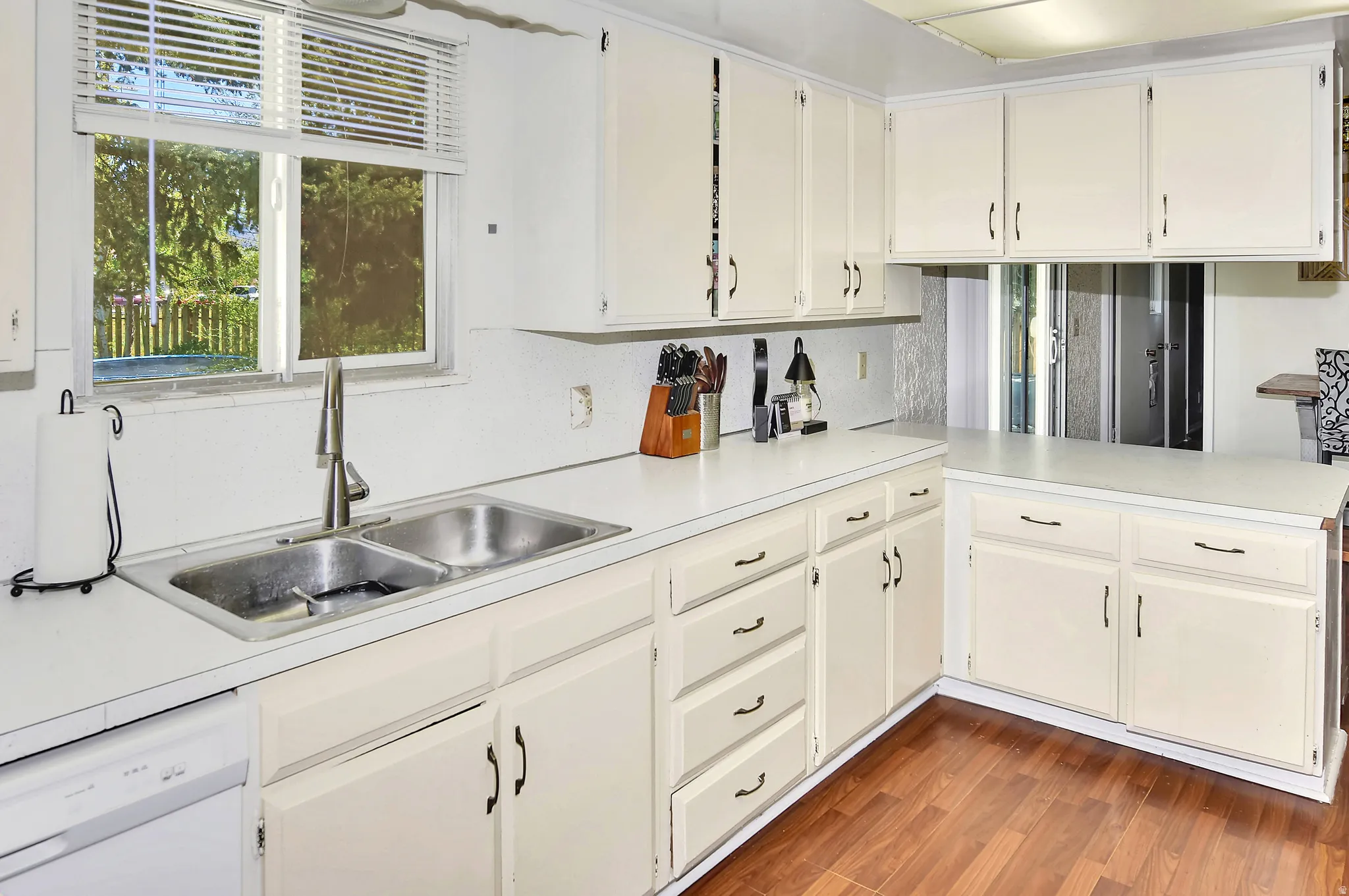 Kitchen featuring white cabinetry, light countertops, a double basin stainless steel sink with a modern faucet, wood-finish flooring, and a window with blinds