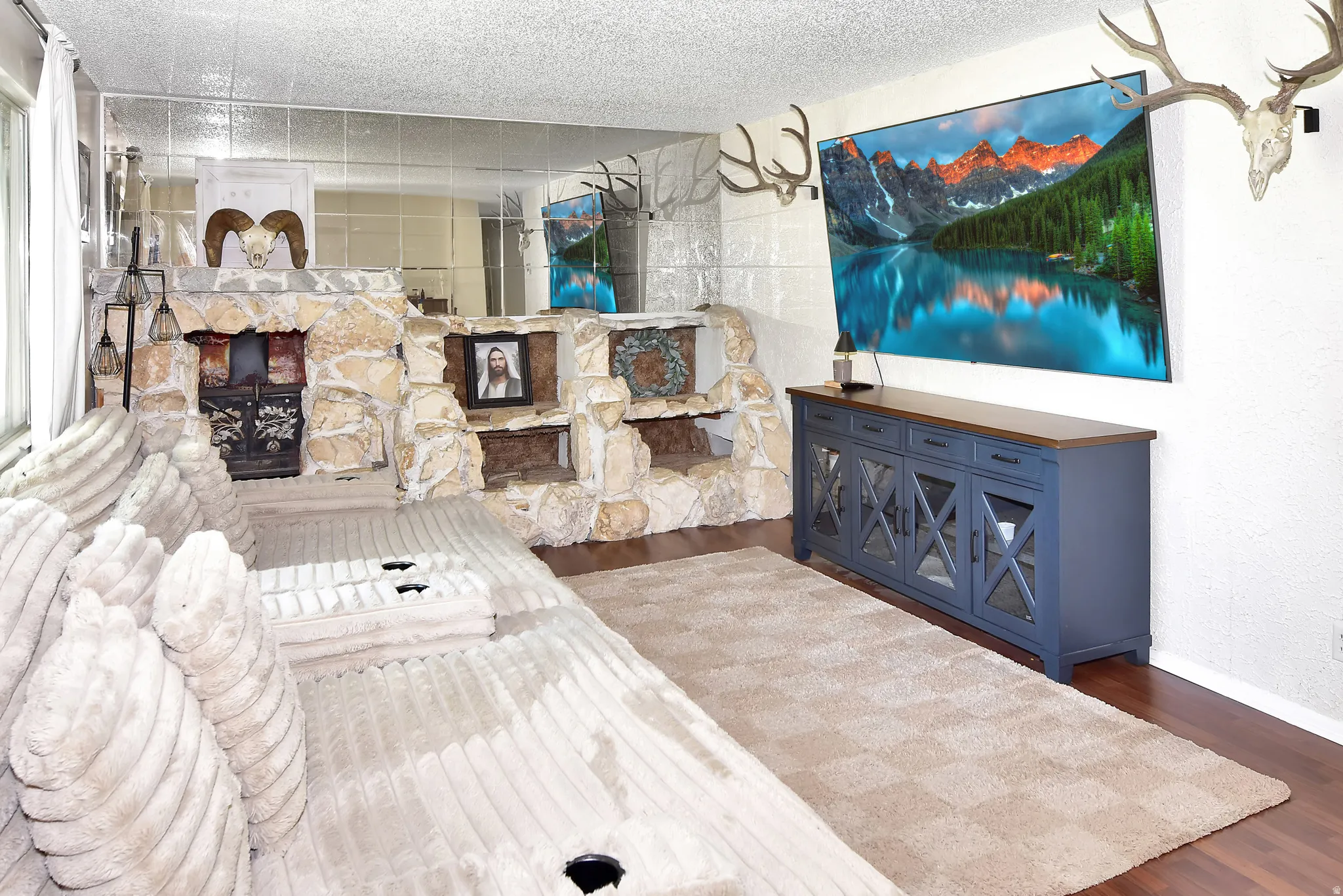 Living area featuring a stone fireplace surround with integrated shelving, wood-finish flooring, and a full wall of mirrored panels