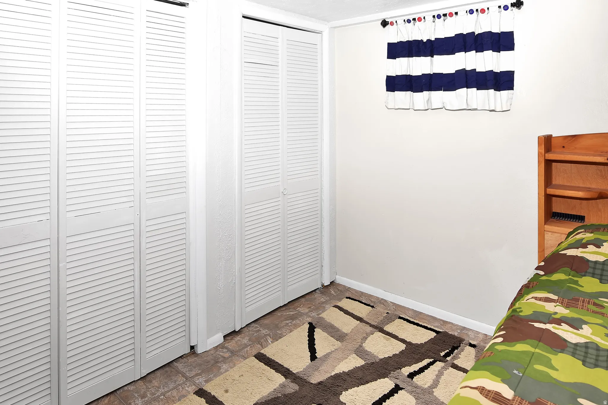 White louvered bi-fold closet doors, tile-finish flooring, and a window with a valance