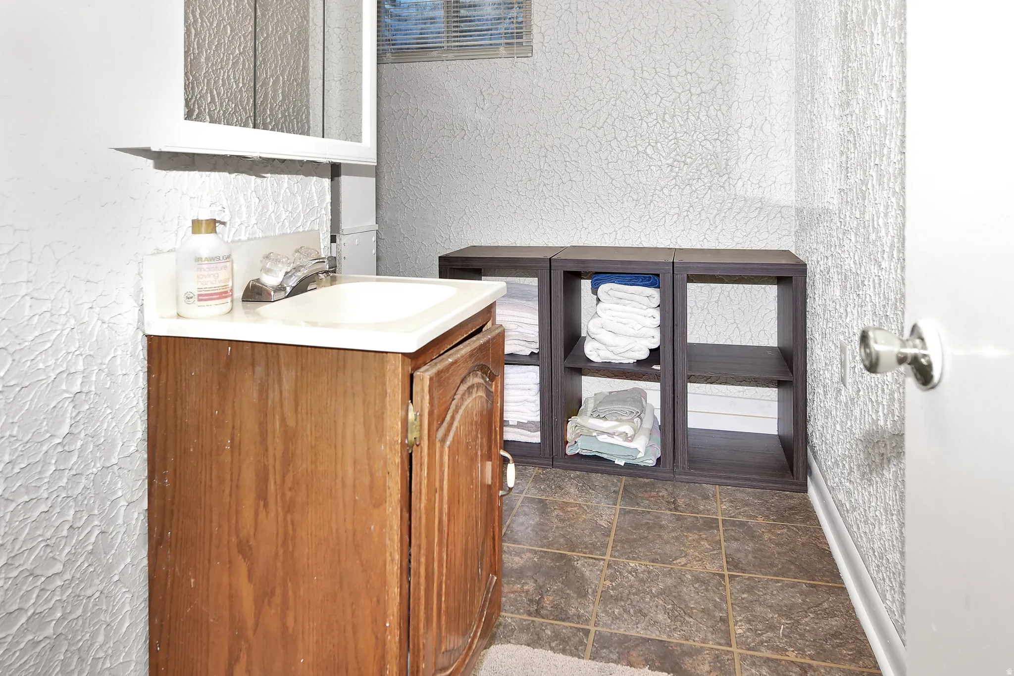 Bathroom vanity with an integrated sink and mirror, featuring textured wall finishes and tiled flooring