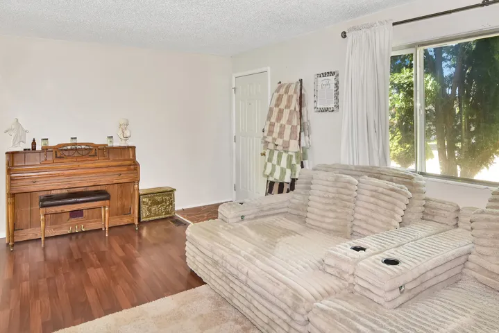Living area featuring wood-finish flooring, white painted walls, and a large window with white curtain panels