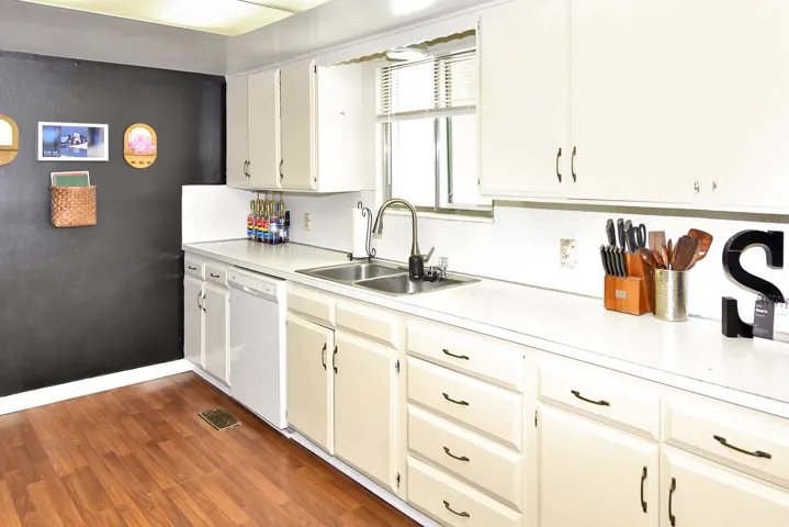 Kitchen featuring wood-finish flooring, white cabinetry, a double basin stainless steel sink, and a white dishwasher