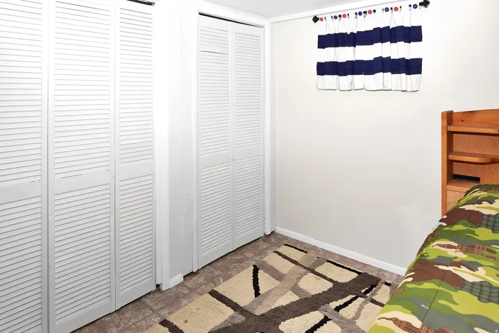 White louvered bi-fold closet doors, tile-finish flooring, and a window with a valance