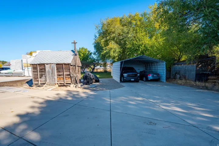 Paved driveway with an open metal carport and mature trees