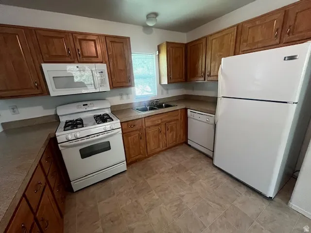 Kitchen featuring wood cabinetry, laminate countertops, a gas range with an overhead microwave, a white refrigerator, and tile-finish flooring
