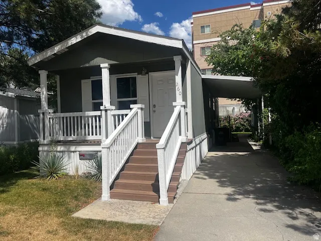 Exterior featuring a covered front porch with white railings, brown-toned steps, and a carport