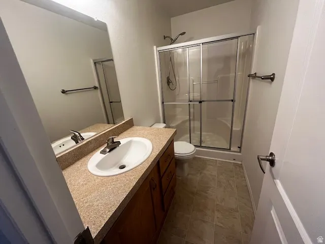 Bathroom featuring a shower with sliding glass doors, a vanity with a drop-in sink, a speckled countertop, and wood-finish cabinetry, all complemented by light-toned flooring