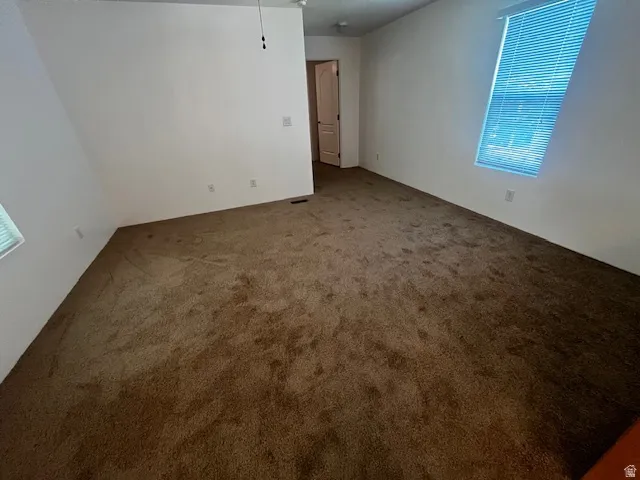 Spacious room featuring neutral wall paint, brown carpet flooring, and a ceiling fan