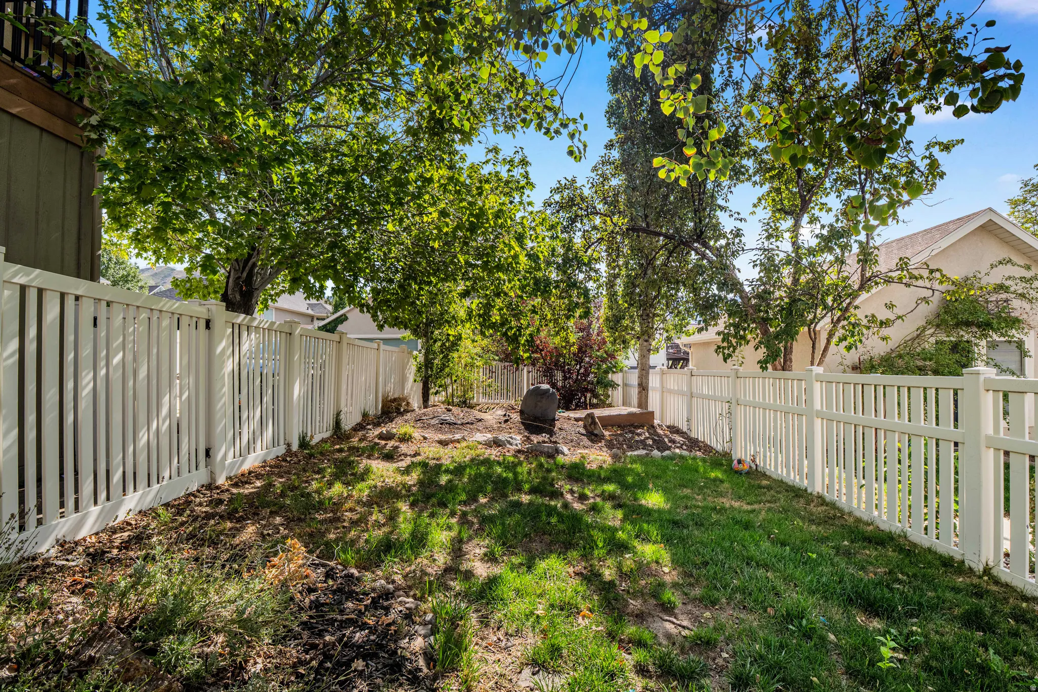 Fenced yard with mature trees and a sloped landscape