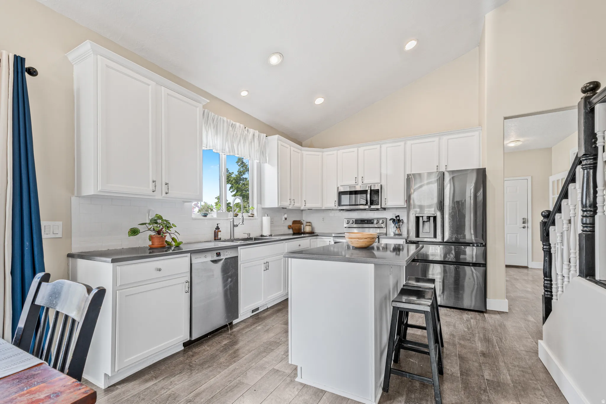Kitchen featuring white cabinetry, dark countertops, stainless steel appliances, wood-finish flooring, and a vaulted ceiling