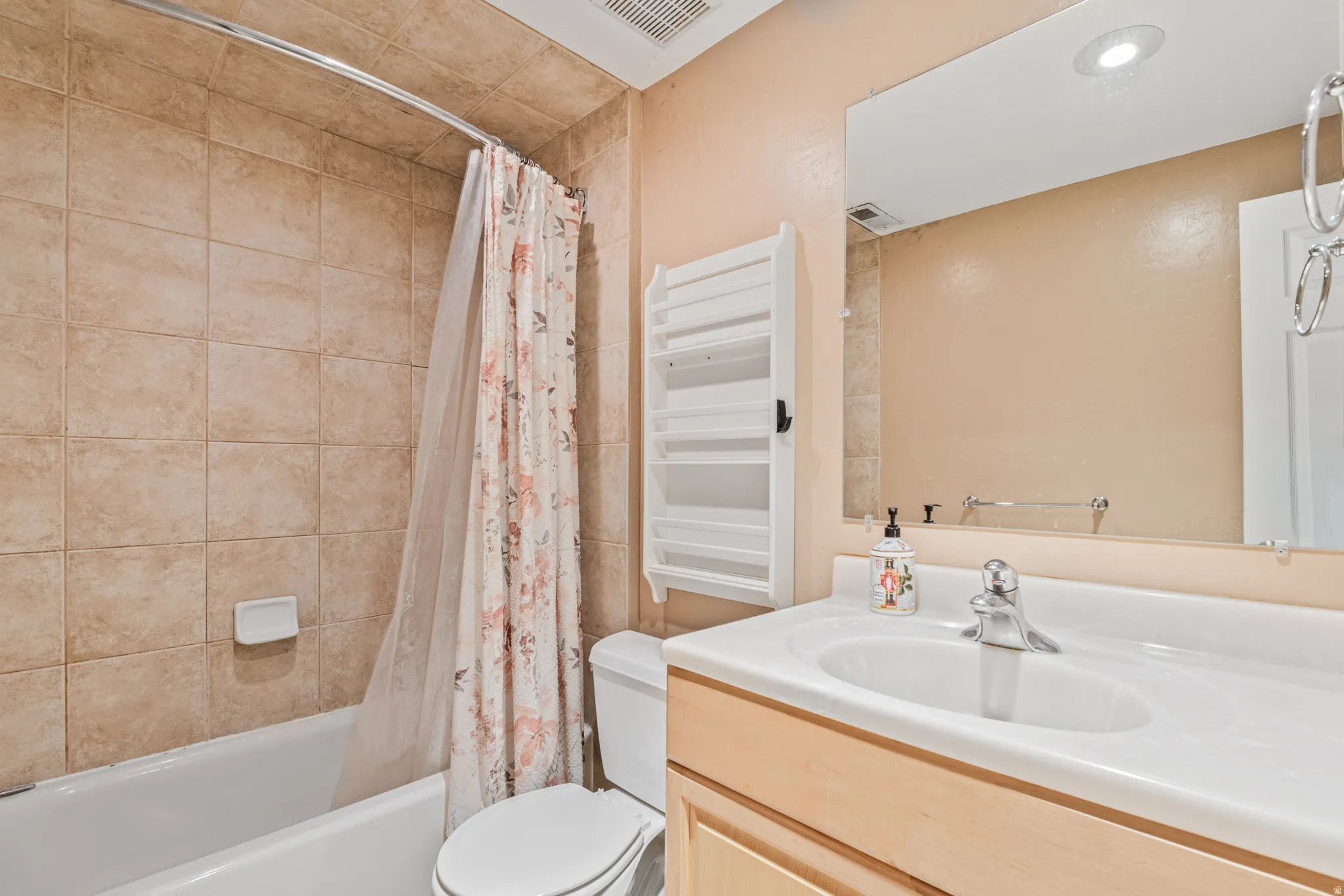 White bathtub with curved shower rod, tile surround, recessed lighting, vanity with integrated sink, and wood-finish cabinetry