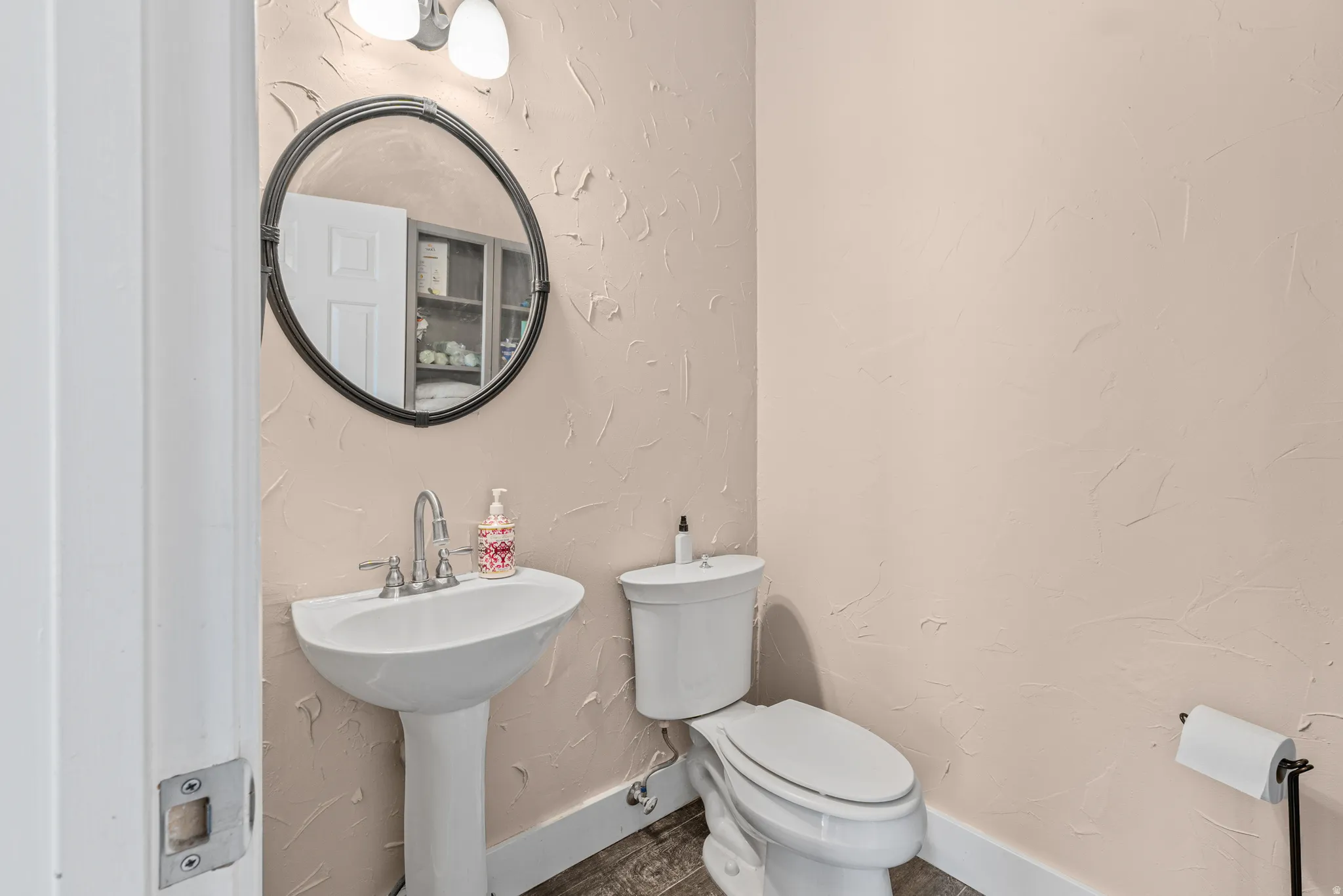 Pedestal sink with a polished chrome faucet, round framed mirror, and two-light vanity fixture
