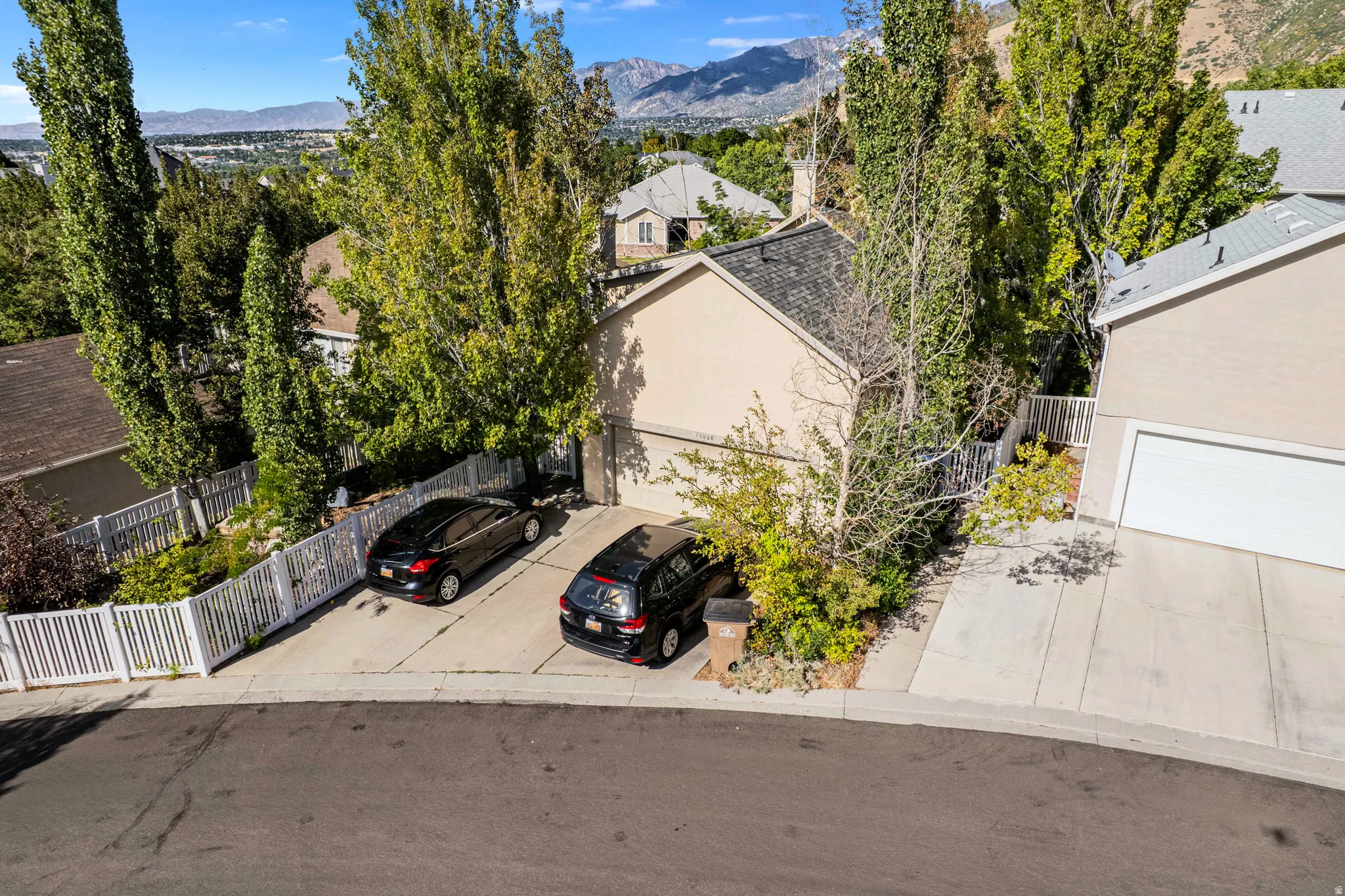 Residential property featuring a paved driveway, attached garage, and mature landscaping