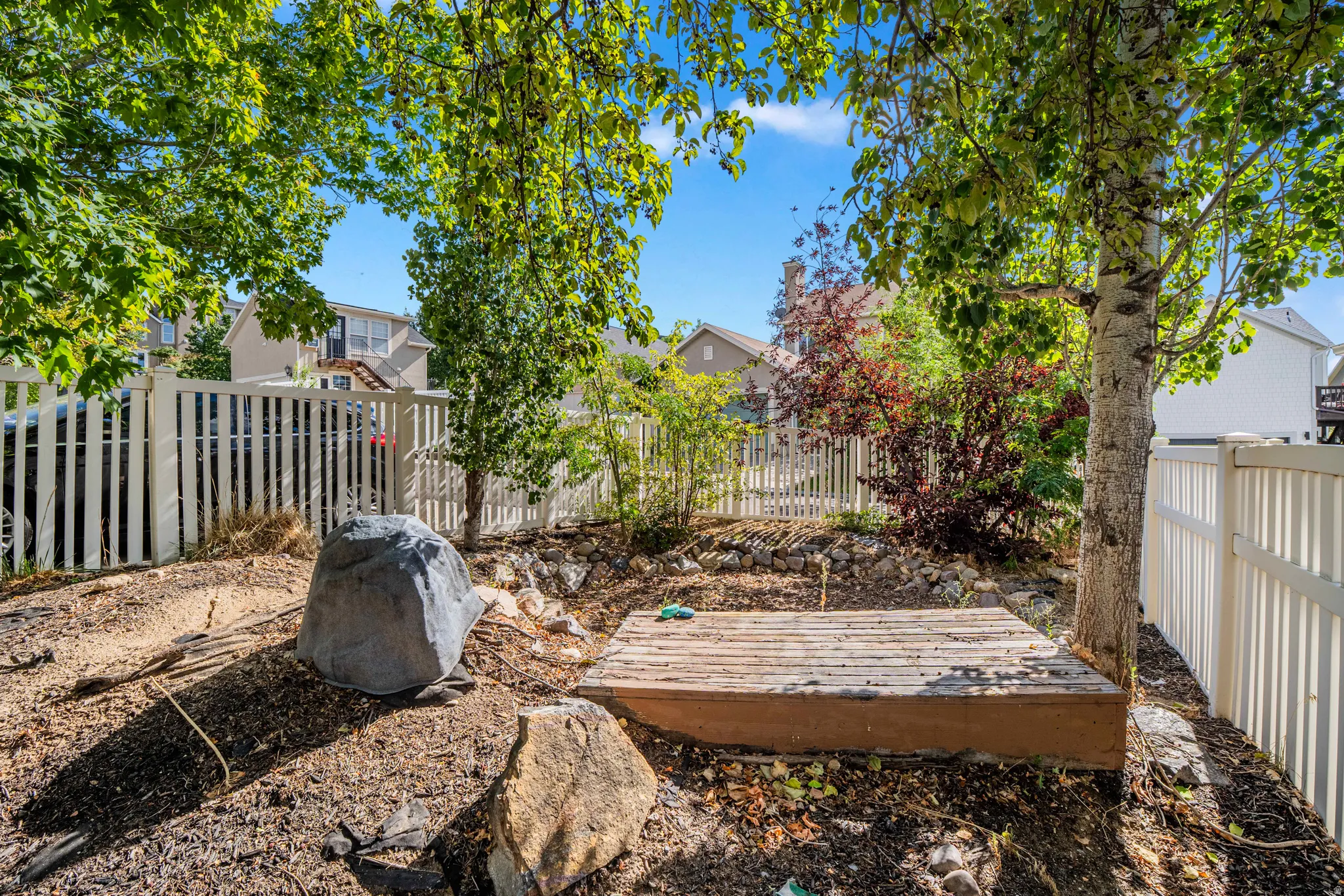 Private backyard space featuring a white picket fence, mature trees, and a wooden platform