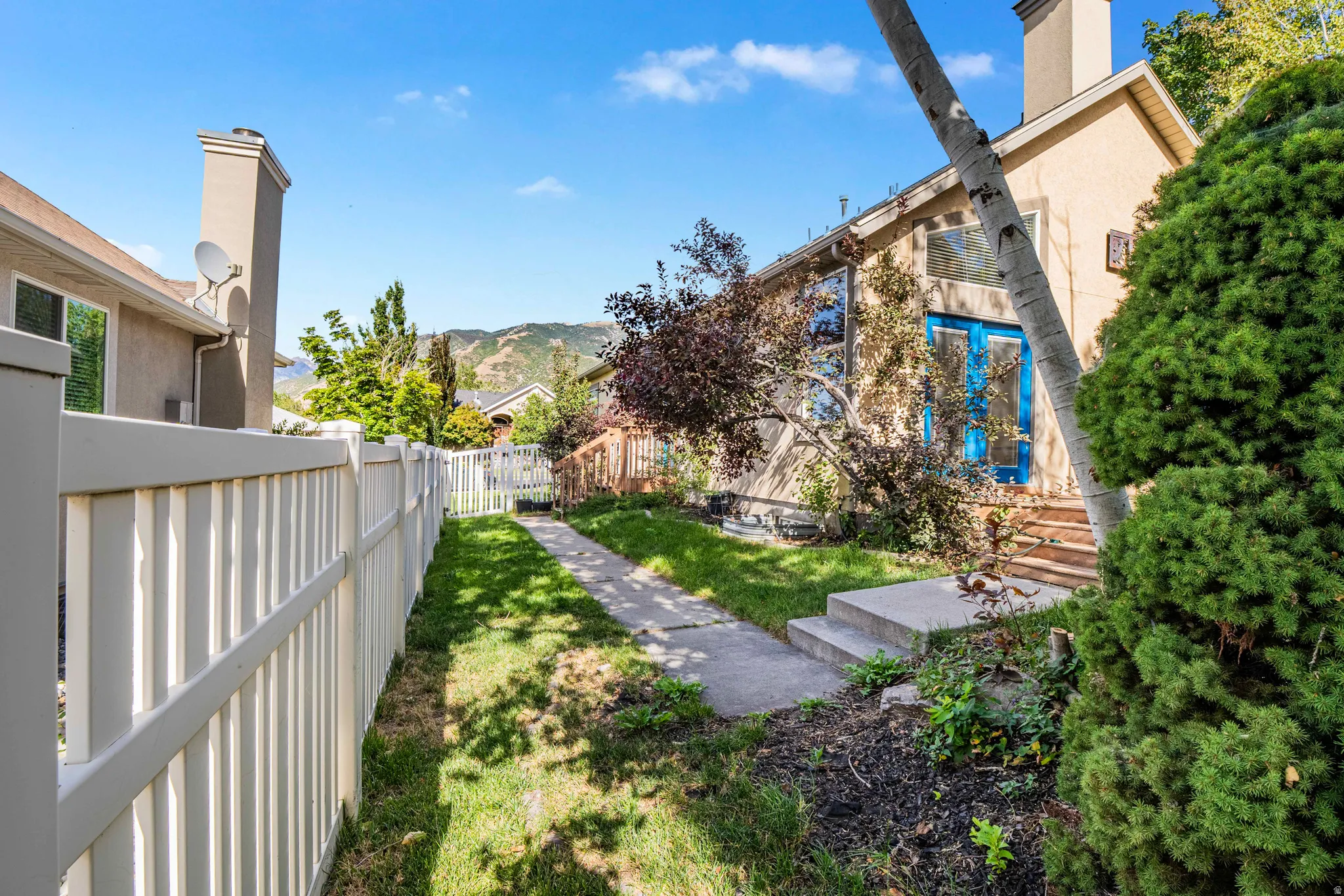 Manicured lawn with a concrete pathway, privacy fencing, mature trees, and a mountain backdrop