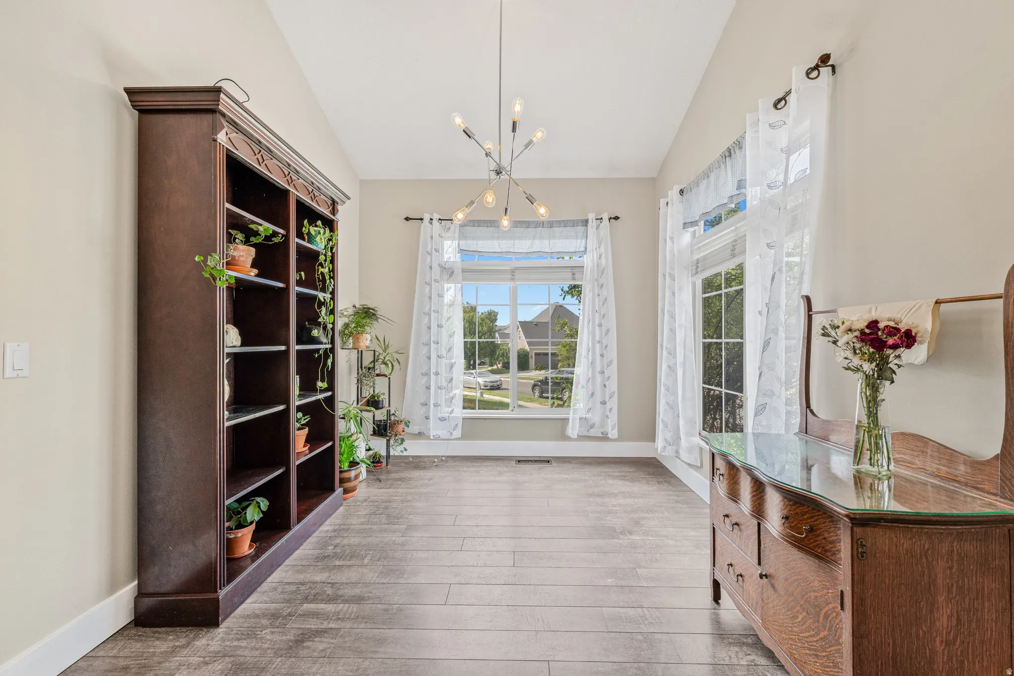 Vaulted ceiling, wood-finish flooring, contemporary chandelier, large windows, and neutral wall tones