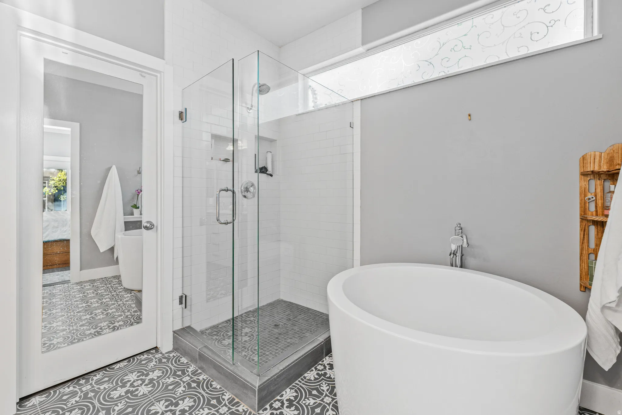 Freestanding soaking tub, glass-enclosed shower, decorative tile flooring, and a transom window
