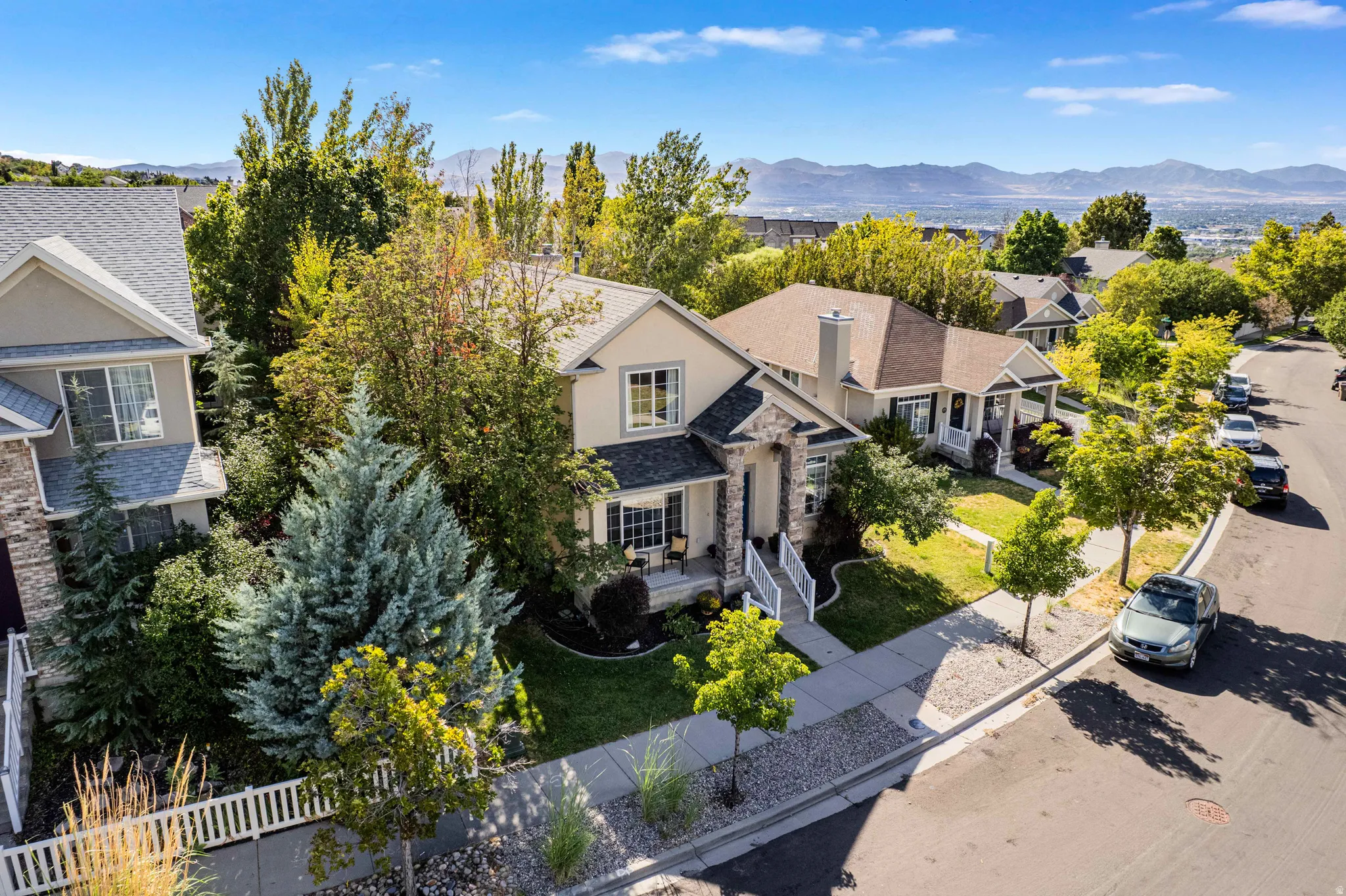 Stucco and stone facade home featuring a covered front porch, mature landscaping, and an attached garage