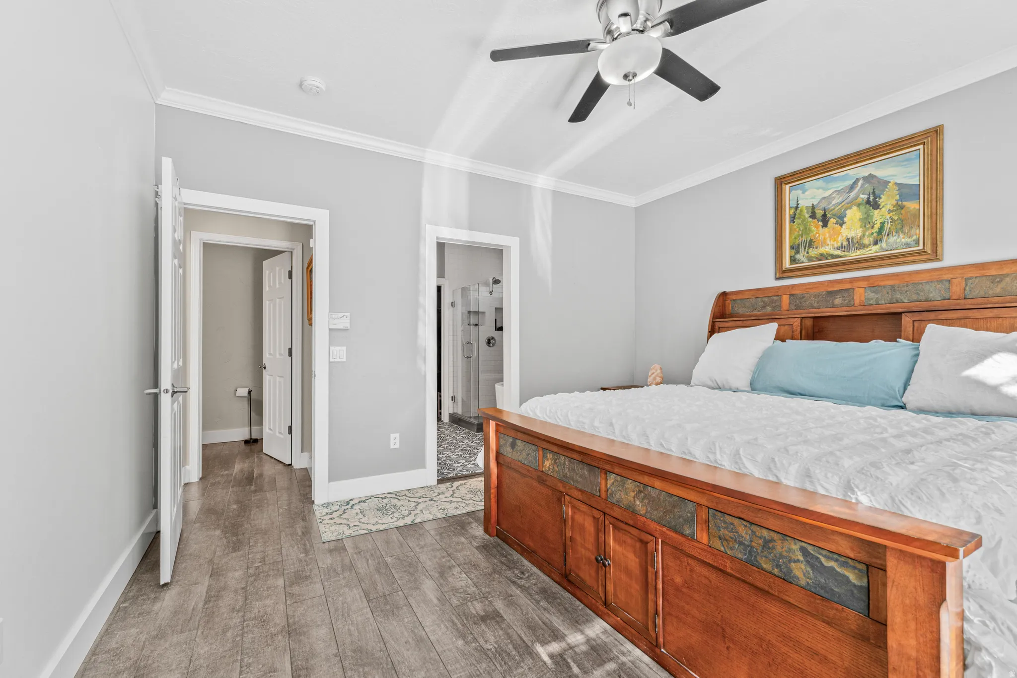Wood-finish flooring throughout, crown molding, ceiling fan with light fixture, and a built-in bed frame with stone accents