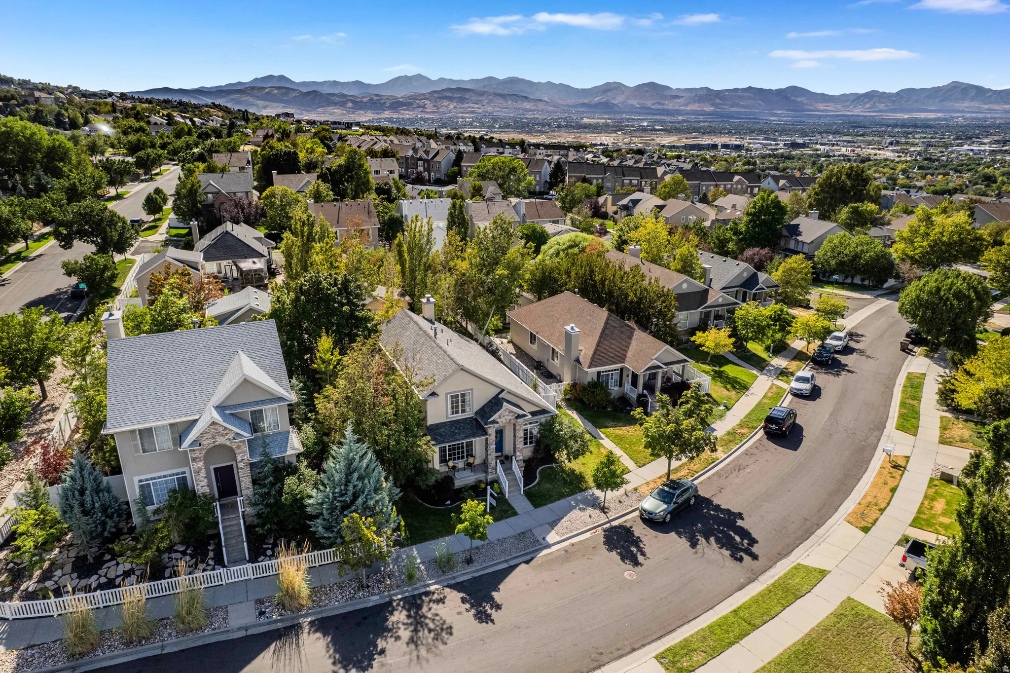 Residential neighborhood with a curved paved road, mature trees, and mountainous background