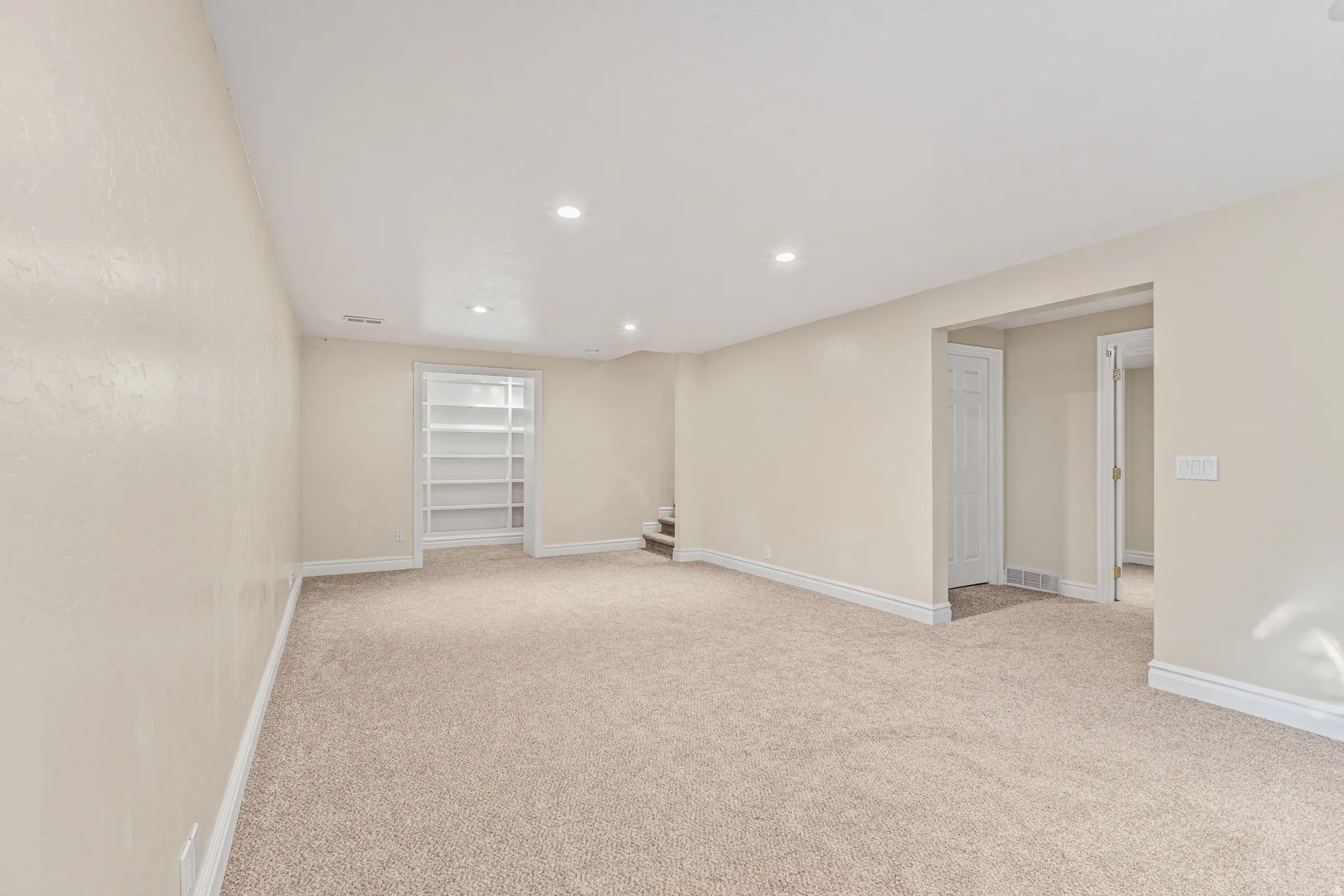Recessed lighting illuminates neutral-toned carpeting and walls