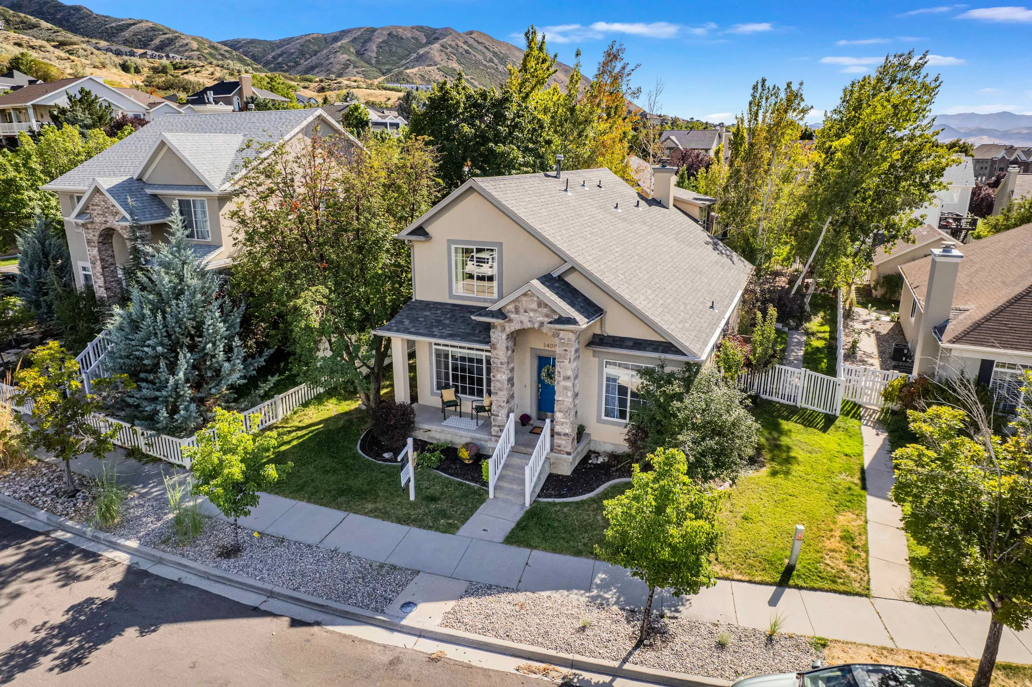 Two-story stucco exterior with stone accents, a covered front porch, a well-maintained lawn, and mature trees