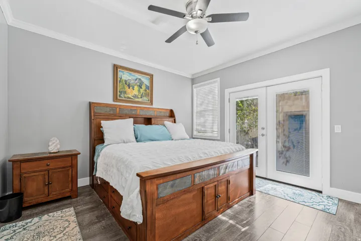 Wood-finish flooring, ceiling fan, white crown molding, white window blinds, and white French doors