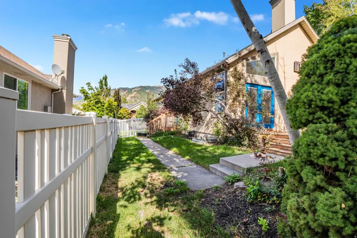 Manicured lawn with a concrete pathway, privacy fencing, mature trees, and a mountain backdrop