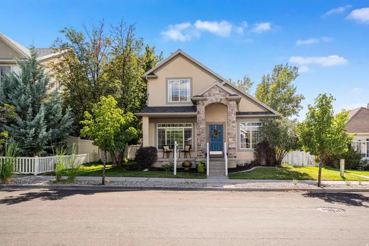 Stucco exterior with stone accents, a blue front door, covered porch, and a white picket fence