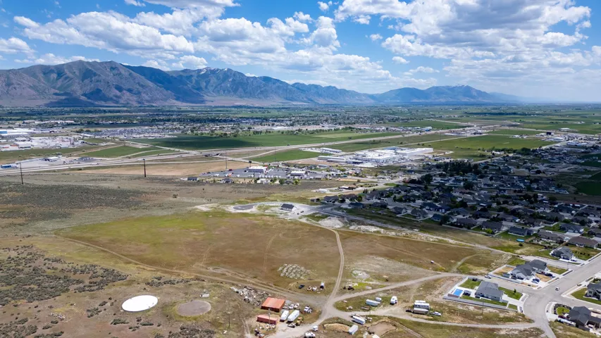 Expansive aerial showcasing a broad landscape with distant mountains, a mix of residential areas, agricultural fields, and undeveloped land