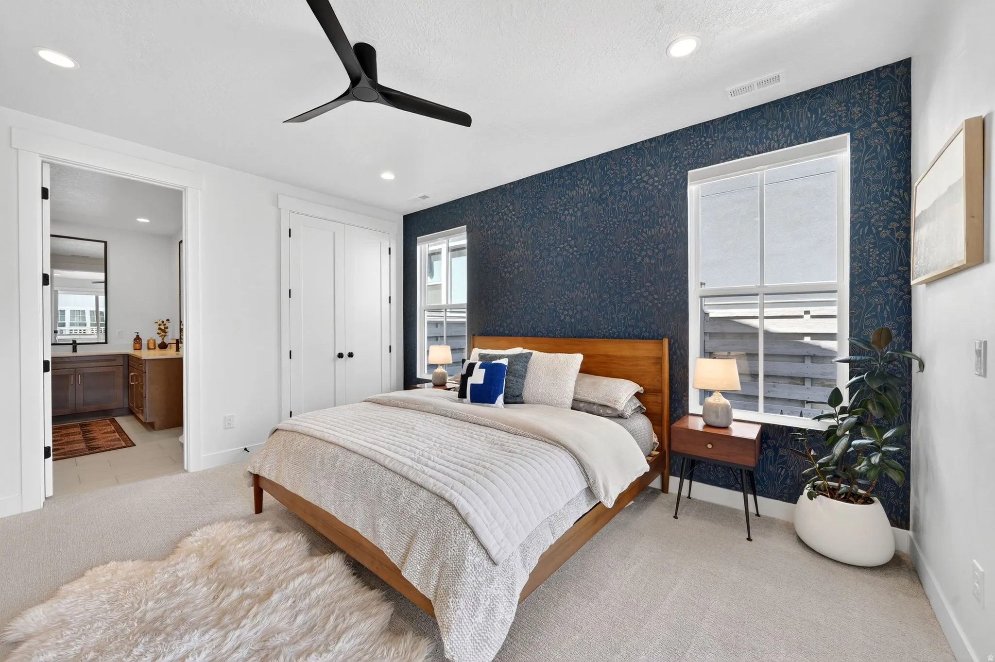 Bedroom featuring a dark accent wall with patterned wallpaper, light-toned carpeting, and a modern black ceiling fan