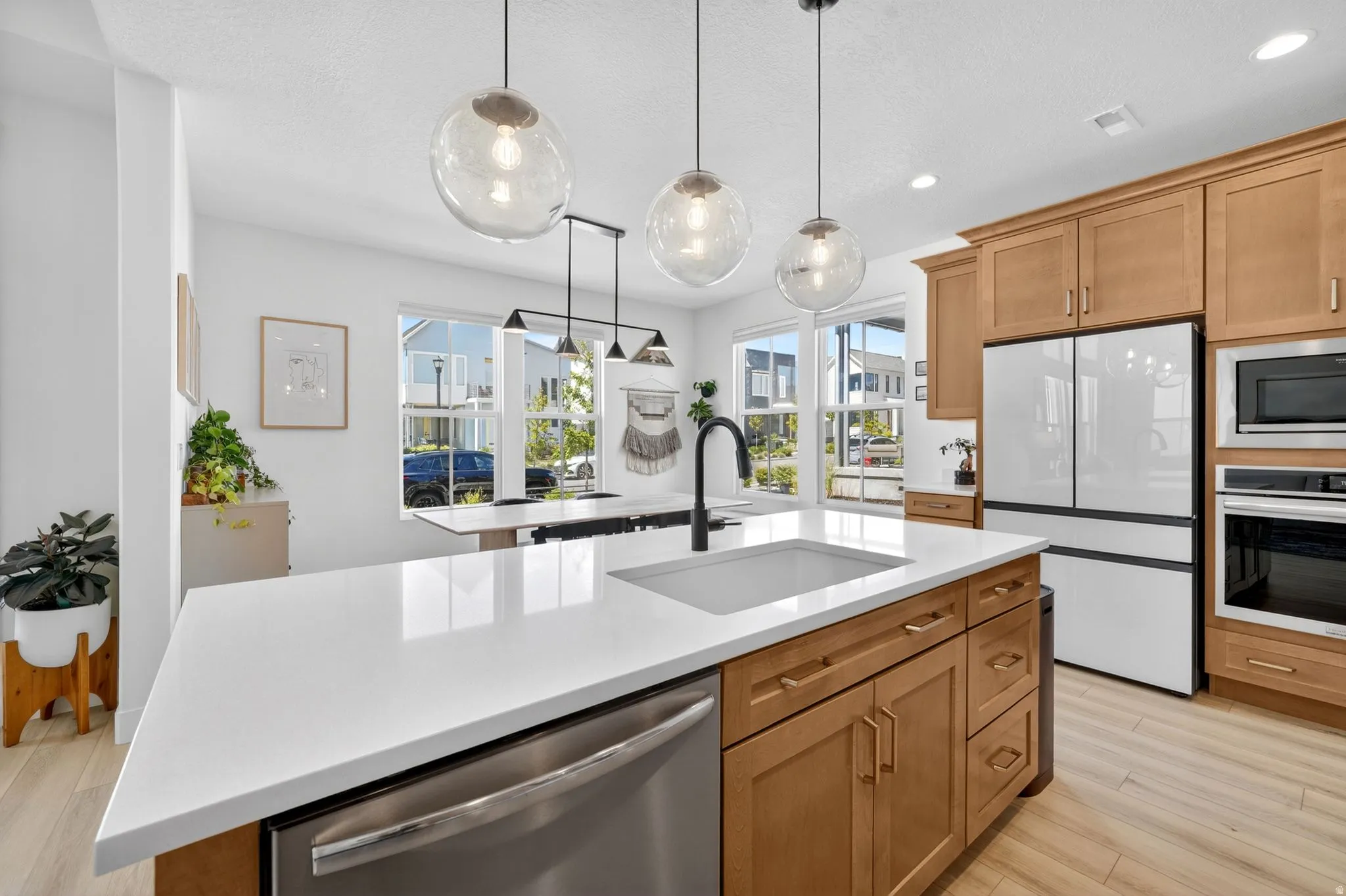 Contemporary kitchen with a central island featuring a white countertop and undermount sink, complemented by light wood-finish cabinetry