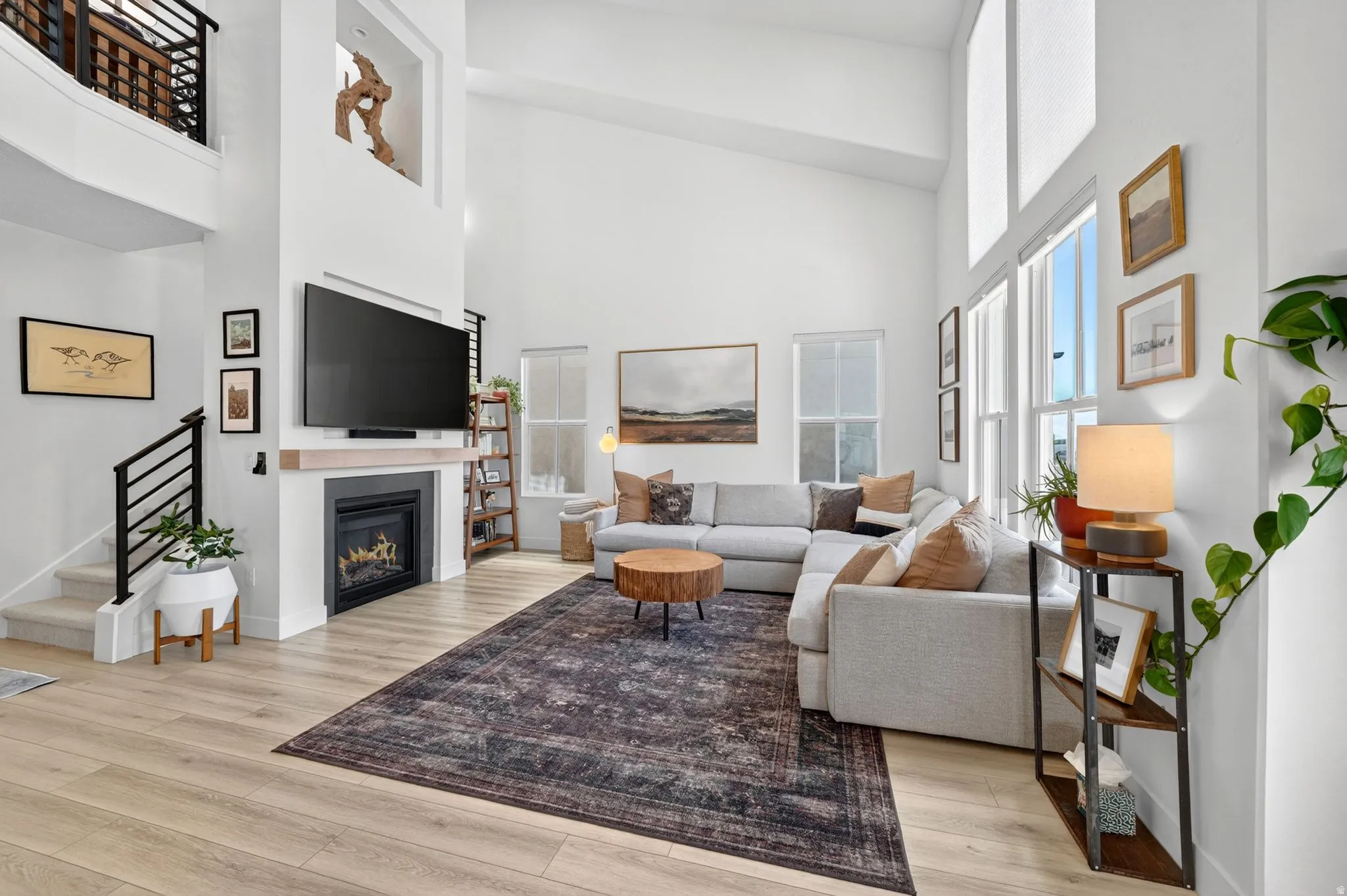 Living area featuring vaulted ceilings, a built-in fireplace with a light wood mantle, wood-finish flooring, and a second-story overlook with a black metal railing