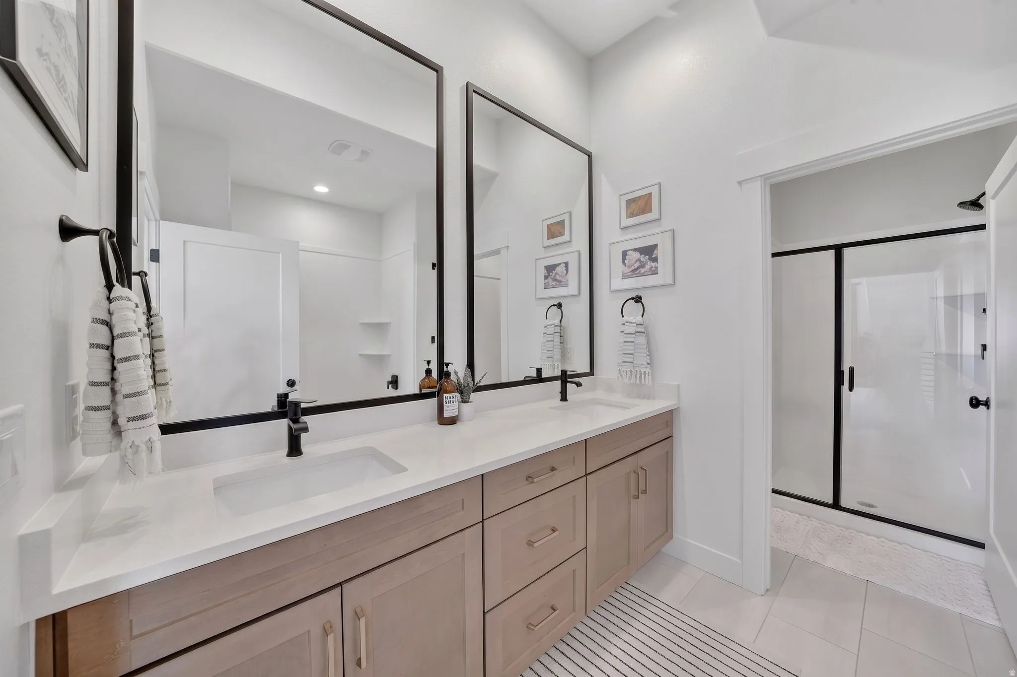 Dual vanity with light wood-finish cabinetry, white countertop, and matte black fixtures