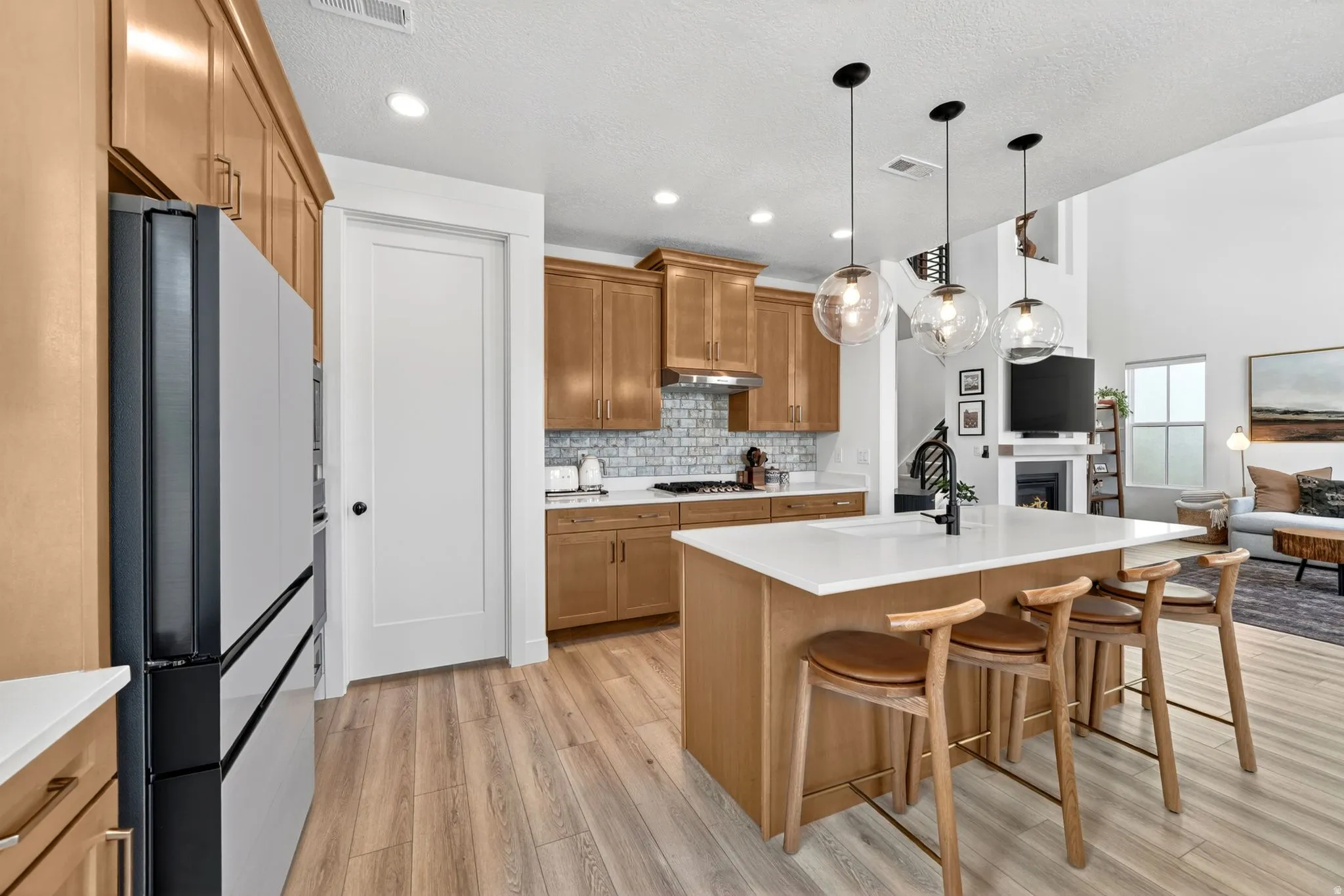 Gourmet kitchen with wood-finish flooring, light wood cabinetry, white subway tile backsplash, and a large island with three pendant lights