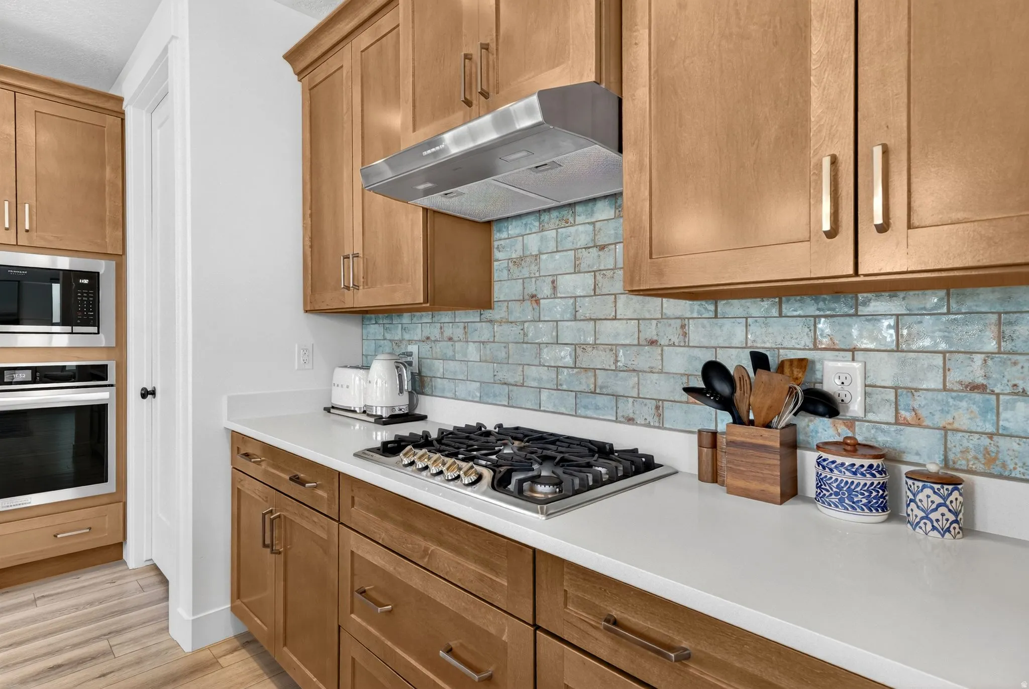 Kitchen featuring stone-finish countertops, natural wood cabinetry, a built-in microwave, an integrated oven, and a gas cooktop with a stainless steel range hood
